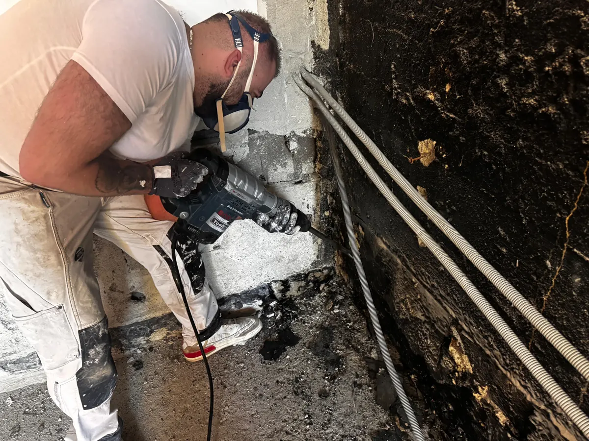 Handwerker stemmt mit dem Bohrhammer den Sockel einer Kellerwand mit alter Bitumenschicht ab, Kellerabdichtung in Innsbruck-Hötting